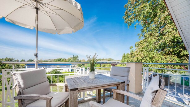 Un espace extérieur aménagé avec des meubles en bois, comprenant une table, des chaises et un parasol, et offrant une vue sur la mer.