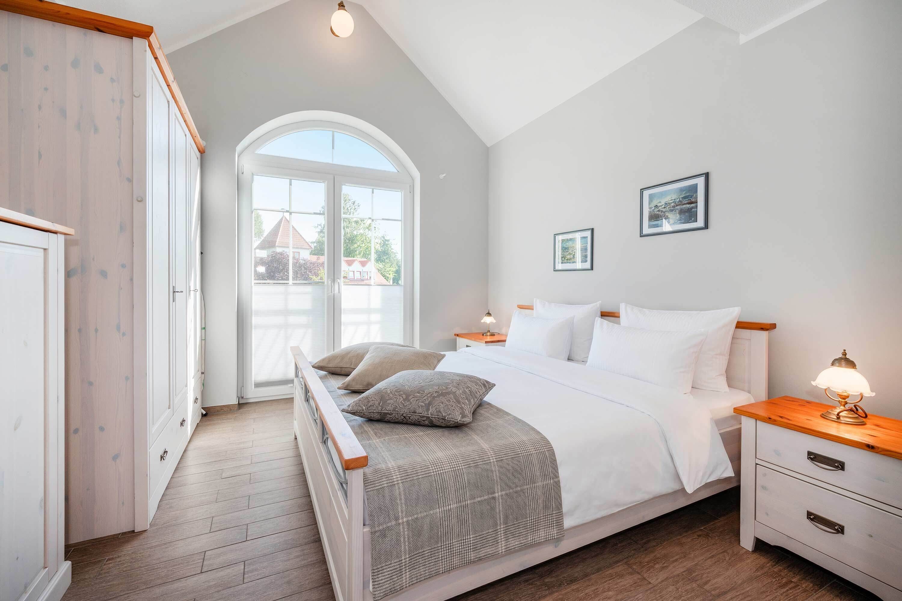 Une chambre à coucher comprenant un lit, des tables de chevet, une armoire et une grande fenêtre.
