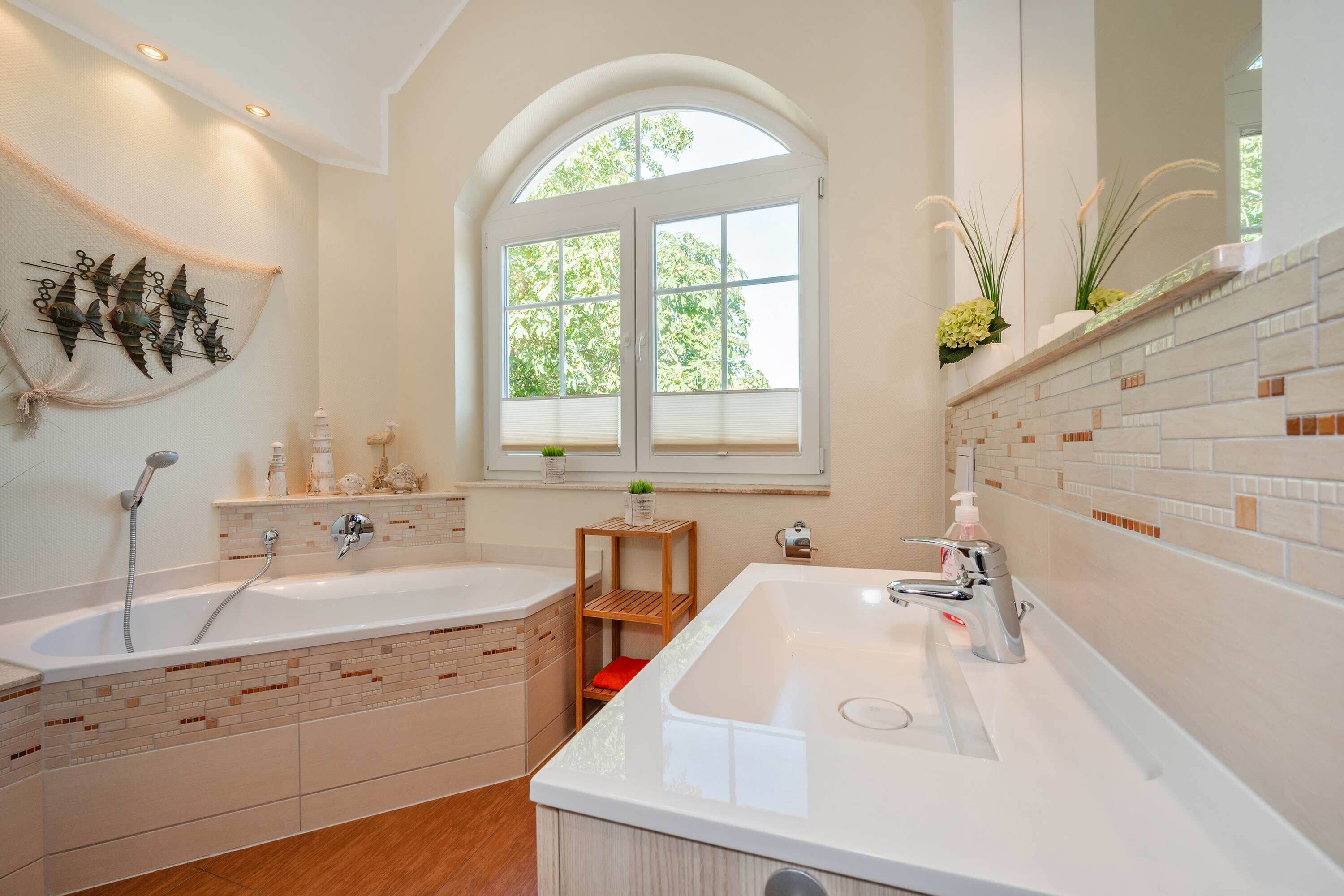 A modern bathroom with a bathtub, a sink, a window, and a mirror.
