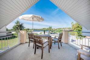 Eine Terrassengaststätte mit Tisch und Stühlen, einem weißen Sonnenschirm und Blick auf die umliegende Natur und die Gebäude.