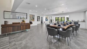 Uma sala de jantar espaçosa e moderna, com uma mesa comprida, cadeiras cinzas e um balcão de recepção de madeira.