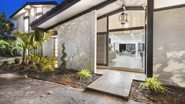 Uma casa moderna com fachada de pedra, porta de entrada de vidro e um terraço com plantas.
