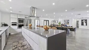 Uma cozinha moderna com eletrodomésticos de aço inoxidável, uma ilha central e um espaço de jantar com uma mesa comprida e cadeiras.