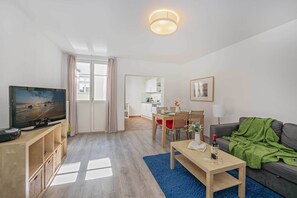 Ein modernes Wohnzimmer mit Fernseher, Couch, Couchtisch und einem Essbereich mit Stühlen.