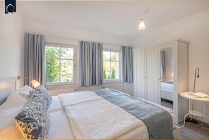 Ein Schlafzimmer mit einem großen Bett, zwei mit Vorhängen versehenen Fenstern, einem Kleiderschrank und einem Nachttisch.