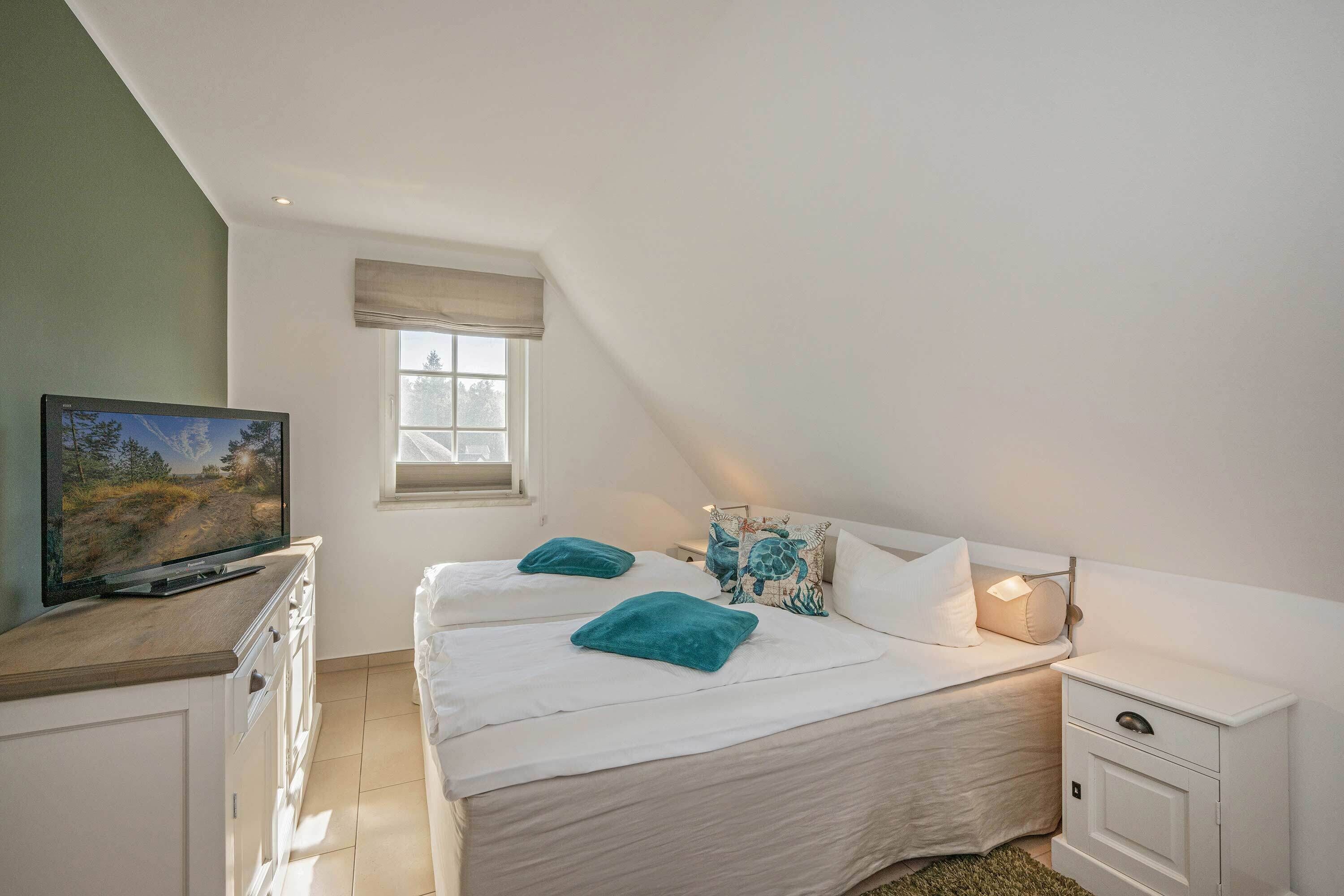 A bedroom with a bed, a TV, a window, and a nightstand.
