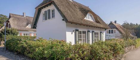Un bâtiment traditionnel avec un toit de chaume, des murs blancs et un mur de pierre agrémenté de verdure.