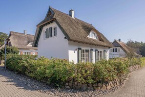 A traditional building with a thatched roof, white walls, and a stone wall with greenery in front. - Modern vacation home with a sauna, garden, and beach access on Usedom (Koserow)