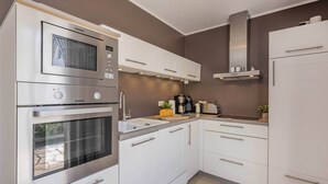 Una cocina con armarios blancos, horno integrado, microondas y cafetera.