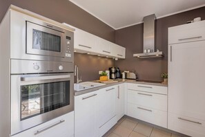 A kitchen with white cabinets, a built-in oven, a microwave, and a coffee maker. - Modern vacation home with a sauna, garden, and beach access on Usedom (Koserow)