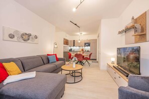 A modern living room with a grey sofa, a dining area with red chairs, a kitchen in the background, and a TV on the right. - Modern vacation rental in Kölpinsee with a balcony—just 600 m from the beach (Ostseebad Kölpinsee)
