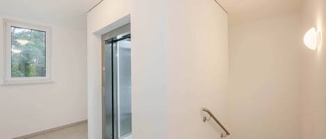 Un interior moderno con una escalera, una puerta que da a un balcón y un ventanal con vistas a árboles.