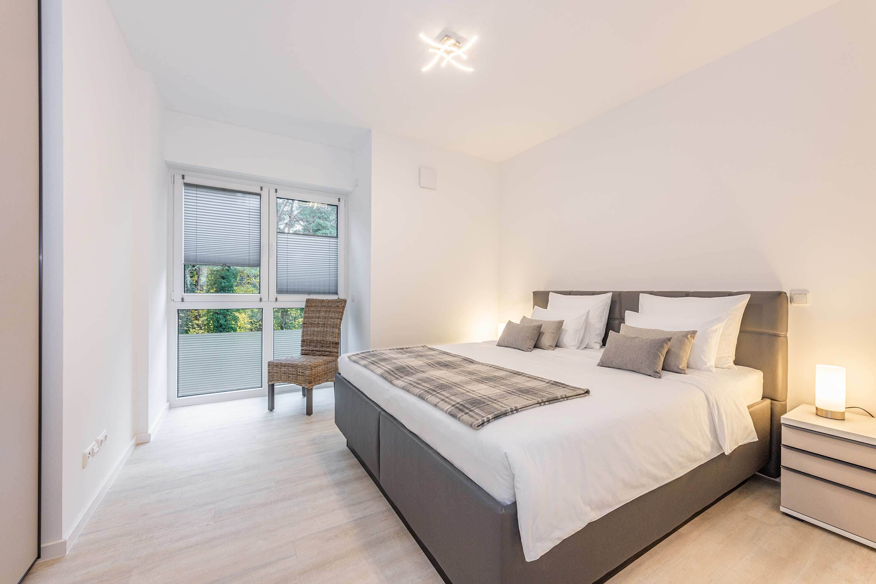Ein Schlafzimmer mit Bett, Nachttisch, Stuhl und einem Fenster mit Jalousien.