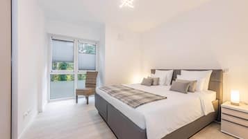 Ein Schlafzimmer mit Bett, Nachttisch, Stuhl und einem Fenster mit Jalousien.