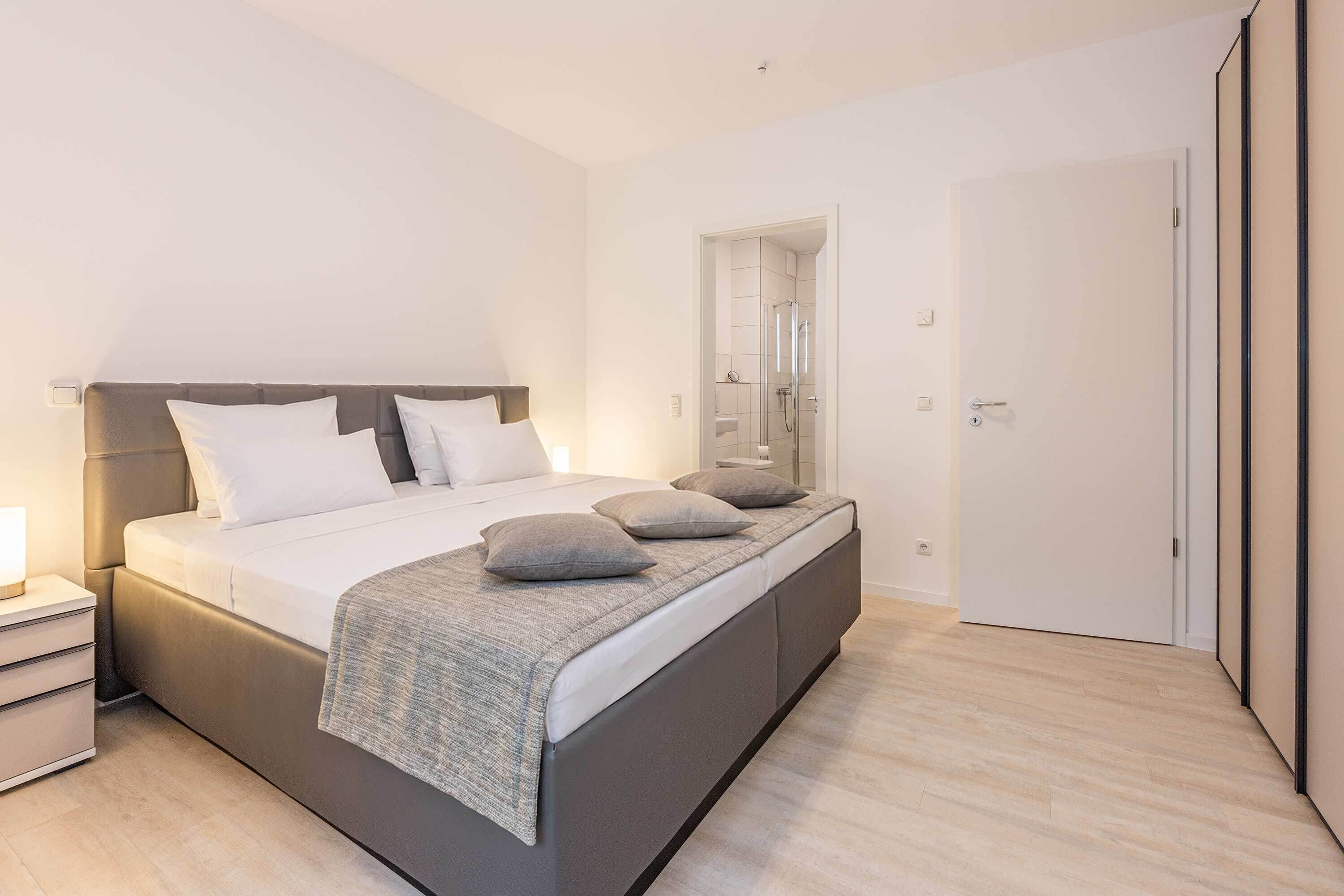 A modern bedroom with a bed, bedside tables, a walk-in closet, and a shower area.