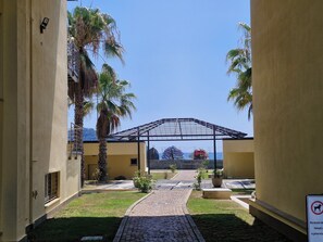 A courtyard with a paved walkway, palm trees, a covered area with a view of the sea, and a no-dog sign. - Albenga Vadino Vista: A prestigious two-room apartment overlooking the sea—a peaceful retreat. (Albenga)