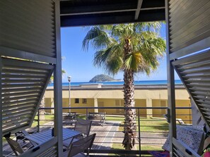 A balcony with a view of the sea, palm trees, and a building in the background. - Albenga Vadino Vista: A prestigious two-room apartment overlooking the sea—a peaceful retreat. (Albenga)