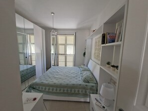 A bedroom with a bed, bedside table, lamp, and a bookshelf. - Albenga Vadino Vista: A prestigious two-room apartment overlooking the sea—a peaceful retreat. (Albenga)