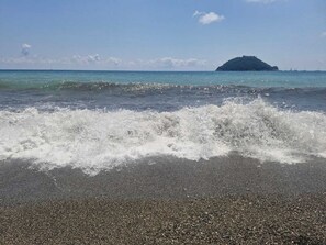 A beach with waves crashing onto the shore and a distant island. - Albenga Vadino Vista: A prestigious two-room apartment overlooking the sea—a peaceful retreat. (Albenga)