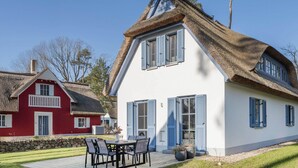 Ein Haus mit einem Strohdach, weißem Anstrich und blauen Fensterläden.
