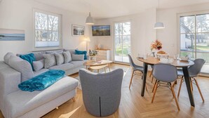 Ein modernes Wohnzimmer mit einem grauen Sofa, einem runden Esstisch und einem grauen Sessel.