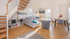 Ein modernes Wohnzimmer mit Treppe, einer Couch, einem Esstisch und einem Bücherregal.