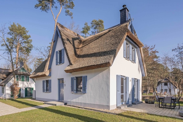 A white building with a steeply pitched roof, blue shutters, and a small porch area. - Modern vacation home with a sauna and garden—quiet and comfortable in a green setting (Zirchow)