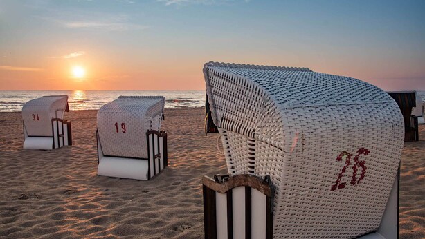 Strandliegen mit Nummern, auf einem Sandstrand angeordnet, mit dem Meer im Hintergrund.