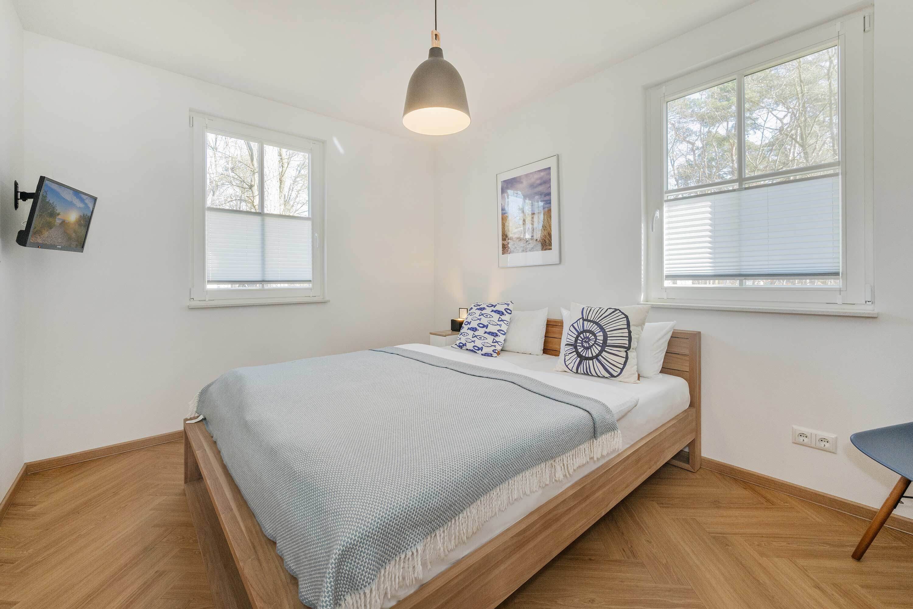 Une chambre à coucher avec un lit, deux fenêtres, un luminaire suspendu et un tableau accroché au mur.