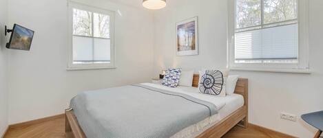 Une chambre à coucher avec un lit, deux fenêtres, un luminaire suspendu et un tableau accroché au mur.