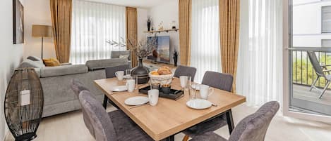 A modern living room with a sofa, a dining table set with plates and glasses, and a large window with curtains.