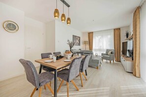 A modern dining area with a wooden table, grey upholstered chairs, and hanging pendant lights. - Modern apartment with a balcony—close to the beach and family-friendly (Ostseebad Kölpinsee)