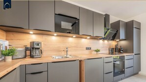 Una cocina moderna con armarios grises, encimera de madera, electrodomésticos integrados e iluminación bajo los armarios.
