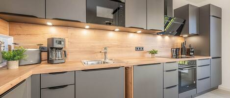 A modern kitchen with grey cabinets, a wooden countertop, built-in appliances, and under-cabinet lighting.