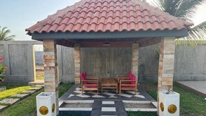 A gazebo with a tiled roof, two wooden tables with chairs, and a checkered floor pattern. - Villa Christopher (Grand Popo)