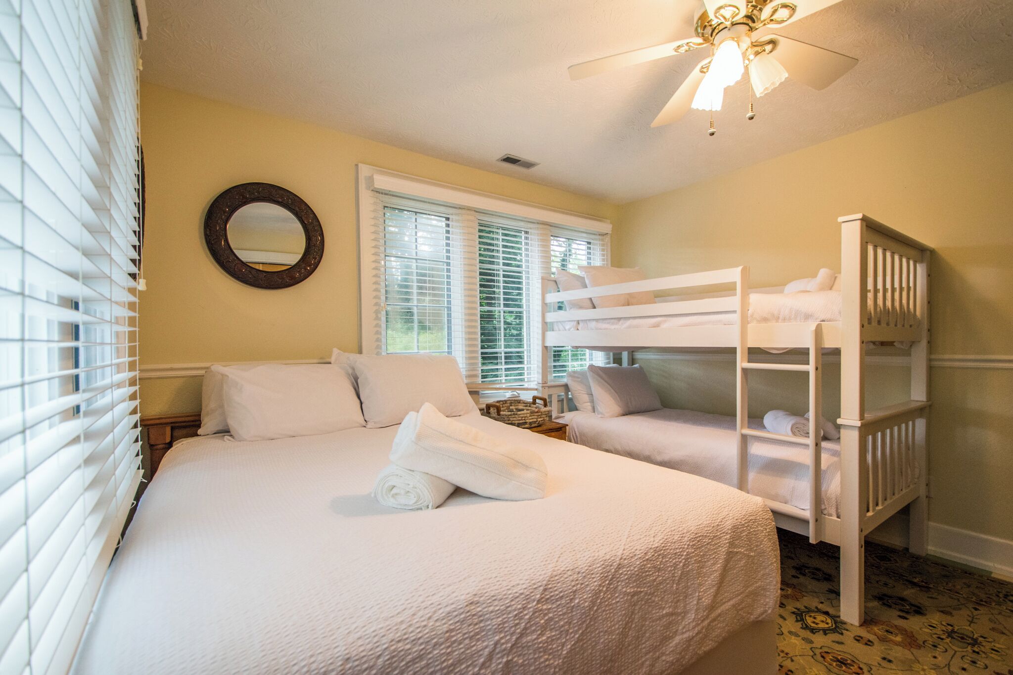 A bedroom with a bunk bed, a single bed, a ceiling fan, and a window with blinds.