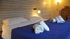 A hotel room with a bed, pillows, a blue bedspread, and rolled towels on the bed. - Deluxe Apartment in Casal Trinacria with a Jacuzzi (Sicilia)