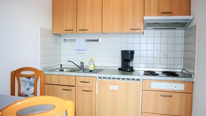 Una cocina compacta con muebles de madera, un lavamanos, una cafetera y una zona de comedor con una silla.
