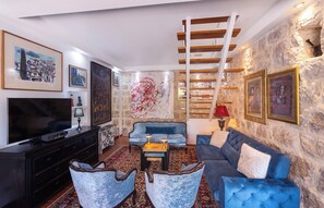 Una sala de estar con televisión, sofá, sillones, obras de arte y una pared de piedra.