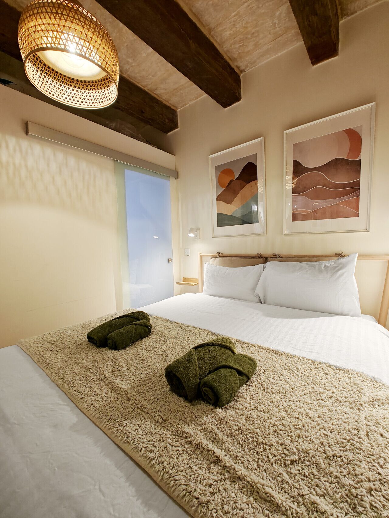 Een hotelkamer met een bed, twee handdoeken, een hanglamp en twee abstracte schilderijen aan de muur.