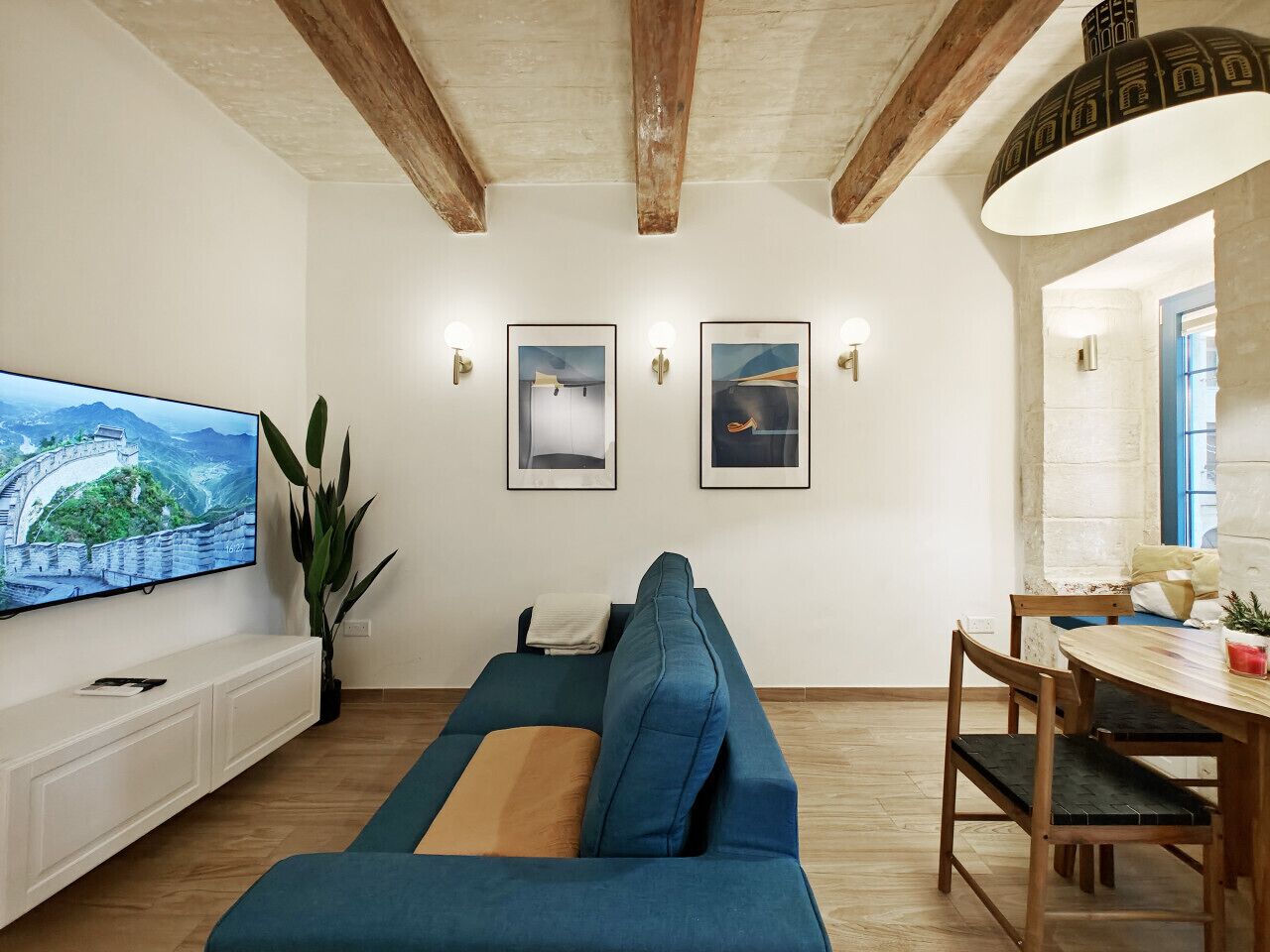 A living room with a sofa, a TV, a dining table, and wall-mounted artwork.