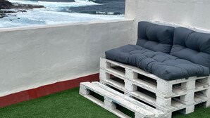 A balcony with a grey cushioned seating area, a concrete wall, and a view of the ocean. - Apartamento con Vistas al Ocenao Atlantico (Santa María de Guía de Gran Canaria)