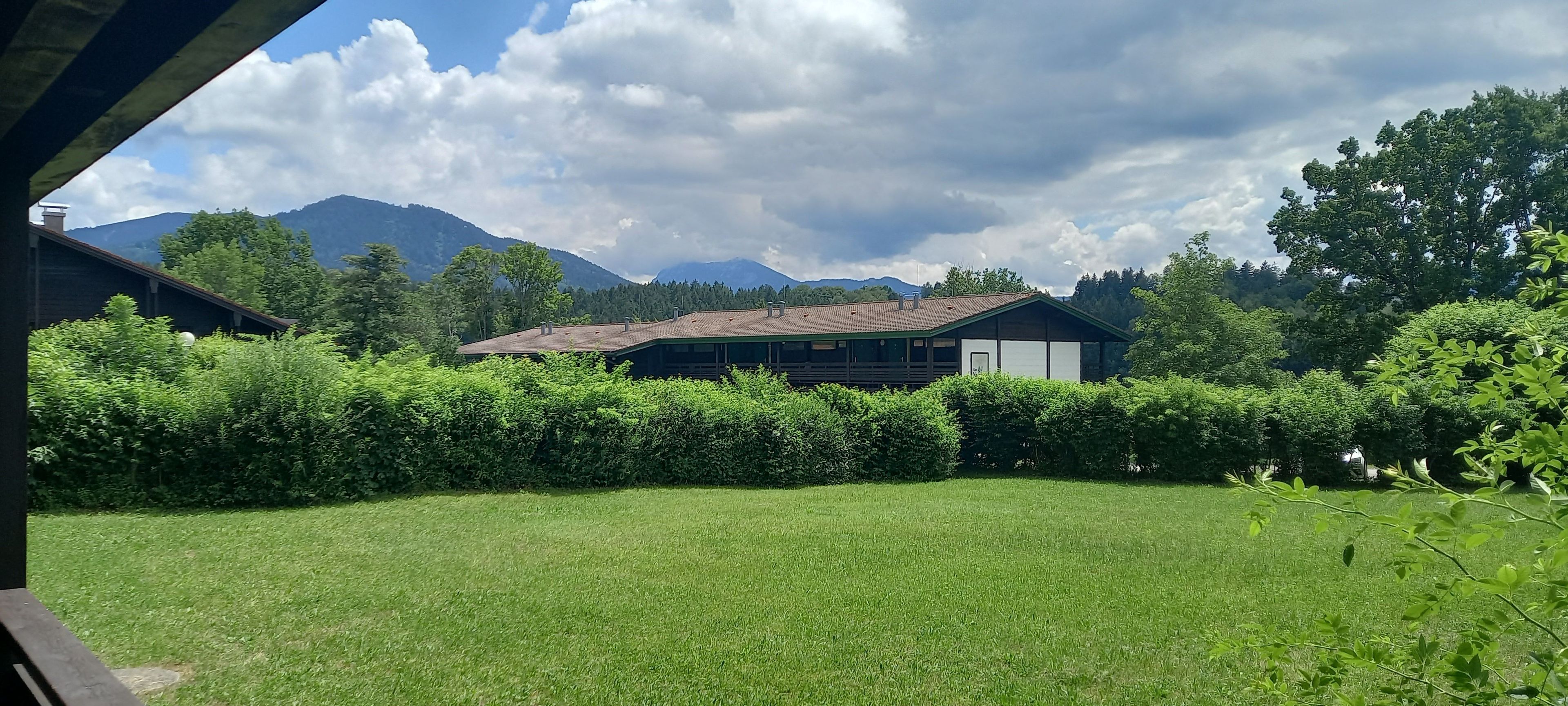 Un bâtiment moderne doté d’un toit en pente, entouré d’une végétation bien entretenue et avec des montagnes en toile de fond.