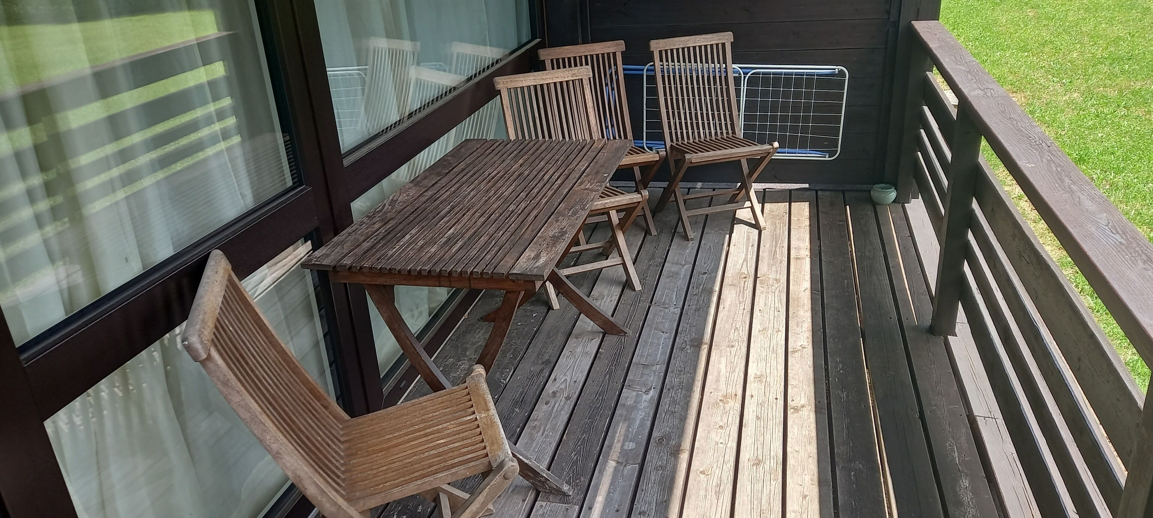 Una terraza de madera con una mesa y sillas, una barandilla metálica y vistas al exterior.