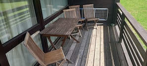 Eine Holzterrasse mit Tisch und Stühlen, einem Metallgeländer und Blick ins Freie.
