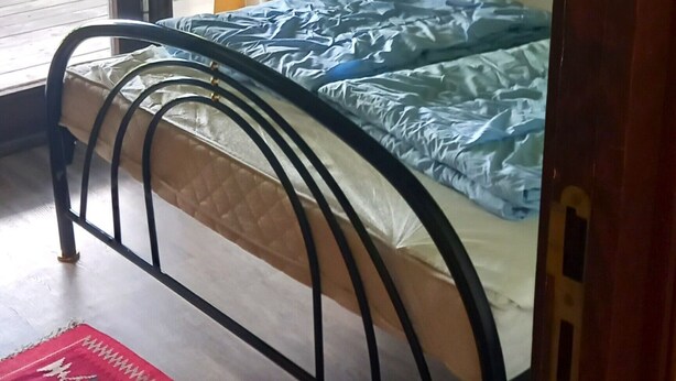 Una habitación con cama, ventana con cortinas, puerta y alfombra estampada.