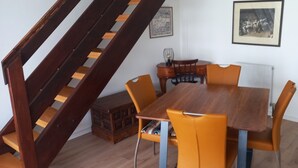Un comedor con mesa de madera y sillas color naranja, una escalera y dos cuadros en la pared.