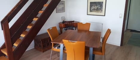 Un comedor con mesa de madera y sillas color naranja, una escalera y dos cuadros en la pared.