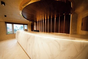 Un mostrador de recepción con encimera de mármol, techo de madera curvada y vistas al exterior a través de un ventanal.