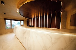 Un mostrador de recepción con encimera de mármol, techo de madera curvada y vistas al exterior a través de un ventanal.